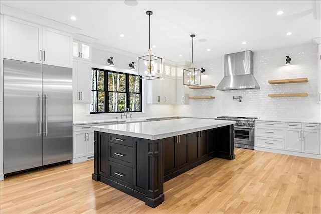 kitchen featuring decorative backsplash, wall chimney exhaust hood, premium appliances, and white cabinets