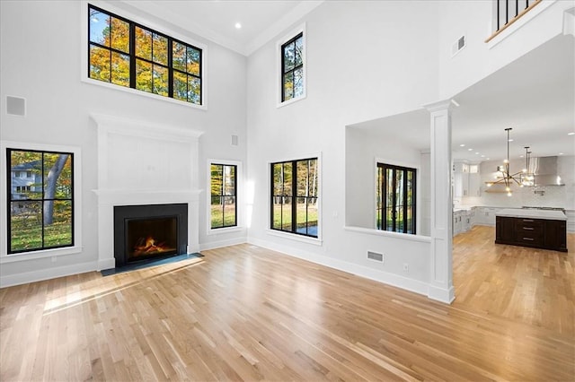 unfurnished living room featuring crown molding, a chandelier, light hardwood / wood-style floors, and a towering ceiling