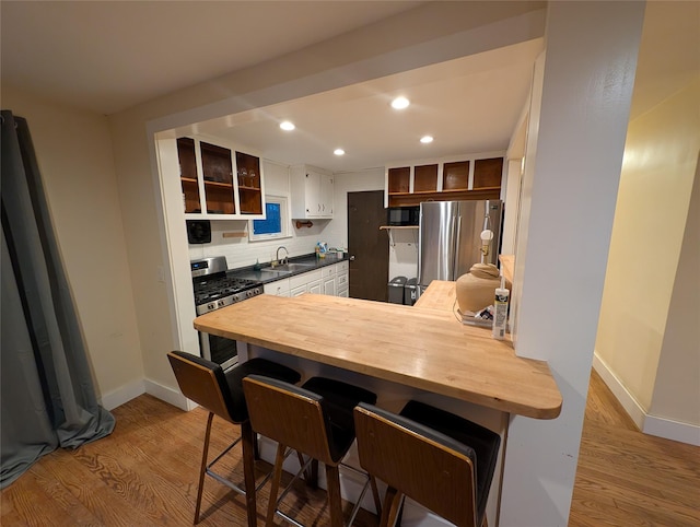 kitchen with kitchen peninsula, backsplash, stainless steel appliances, sink, and light hardwood / wood-style floors