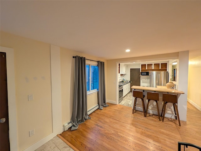 kitchen featuring black microwave, white cabinetry, baseboard heating, stainless steel fridge, and a kitchen bar