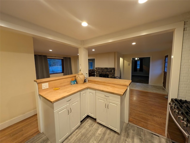 kitchen with butcher block counters, white cabinetry, kitchen peninsula, high end stainless steel range, and light wood-type flooring