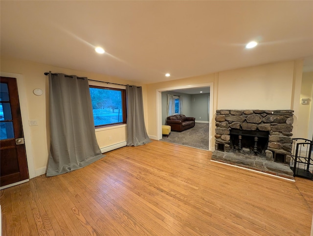 living room featuring a stone fireplace, a baseboard radiator, and light wood-type flooring