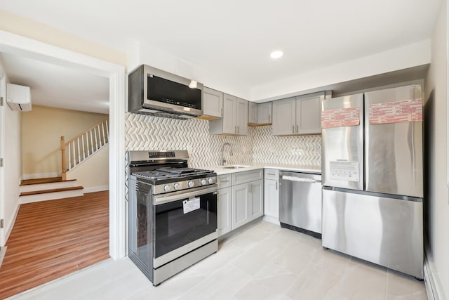 kitchen with a sink, stainless steel appliances, gray cabinetry, backsplash, and a wall mounted AC