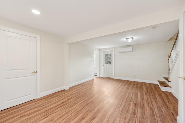 unfurnished room featuring light wood finished floors, recessed lighting, stairway, an AC wall unit, and baseboards