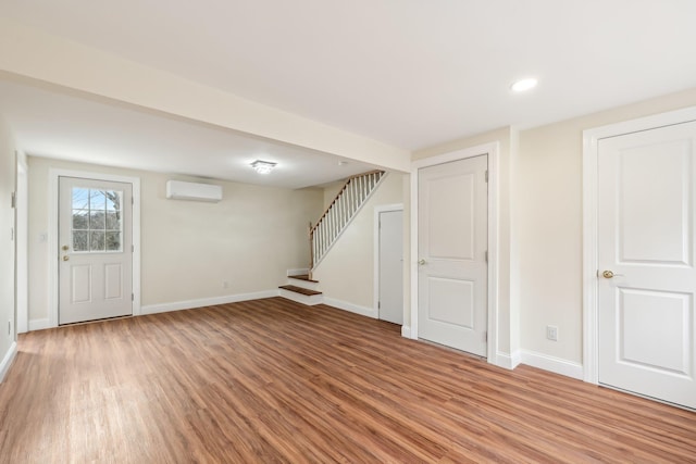 below grade area featuring light wood-style flooring, stairs, baseboards, and an AC wall unit