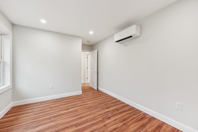 spare room with an AC wall unit, light wood-style floors, recessed lighting, and baseboards