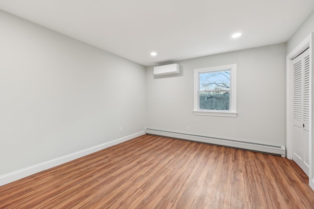 unfurnished bedroom with a baseboard radiator, a closet, a wall mounted AC, wood finished floors, and baseboards