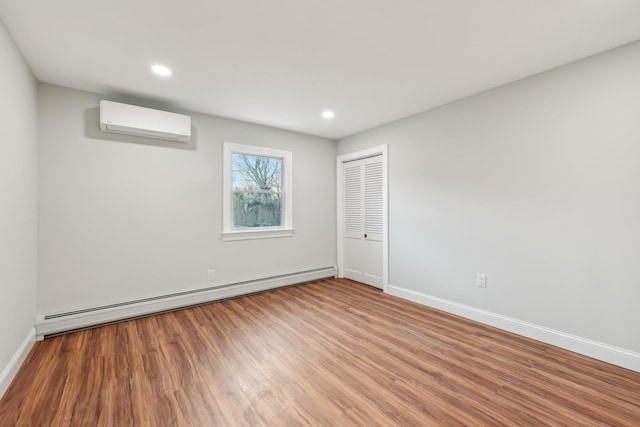 interior space with a baseboard radiator, wood finished floors, baseboards, an AC wall unit, and a closet