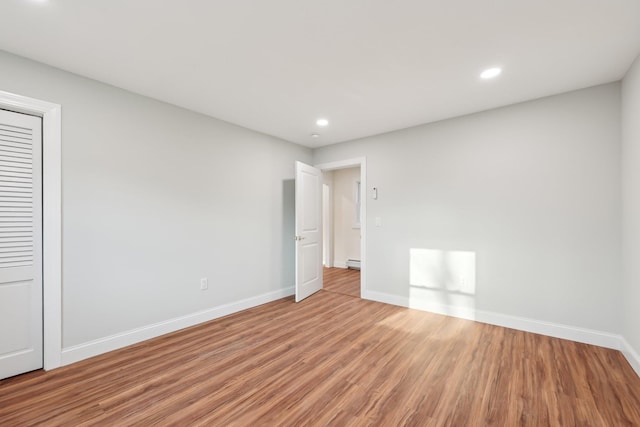 empty room with a baseboard heating unit, recessed lighting, light wood-type flooring, and baseboards