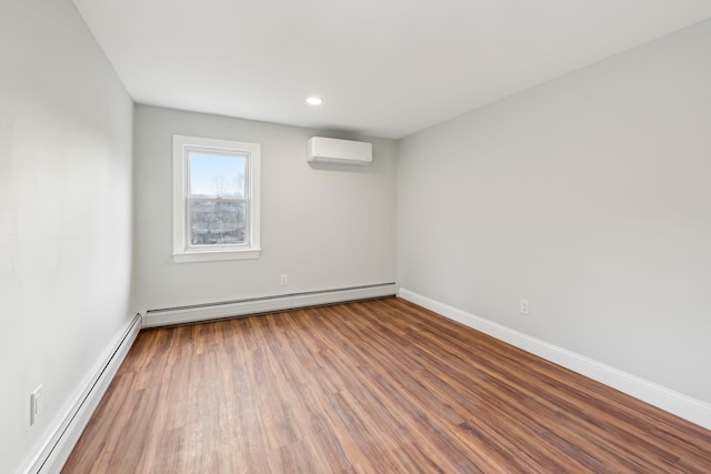 spare room featuring a baseboard heating unit, a wall unit AC, wood finished floors, and baseboards