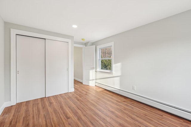 unfurnished bedroom featuring recessed lighting, a closet, baseboard heating, wood finished floors, and baseboards