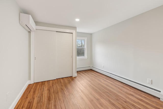 unfurnished bedroom with baseboards, a wall unit AC, light wood-style floors, a baseboard heating unit, and a closet