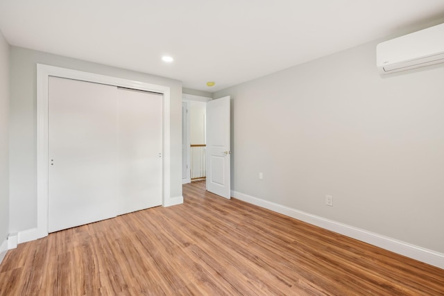 unfurnished bedroom featuring a wall unit AC, light wood finished floors, recessed lighting, a closet, and baseboards