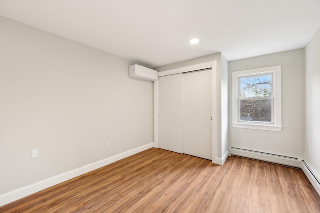 unfurnished bedroom featuring light wood-style floors, a baseboard radiator, baseboards, and a wall mounted AC