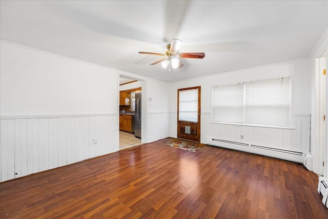 empty room with ceiling fan, light wood-type flooring, baseboard heating, and ornamental molding