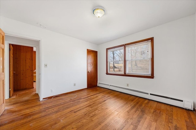 unfurnished bedroom with a baseboard heating unit and light wood-type flooring