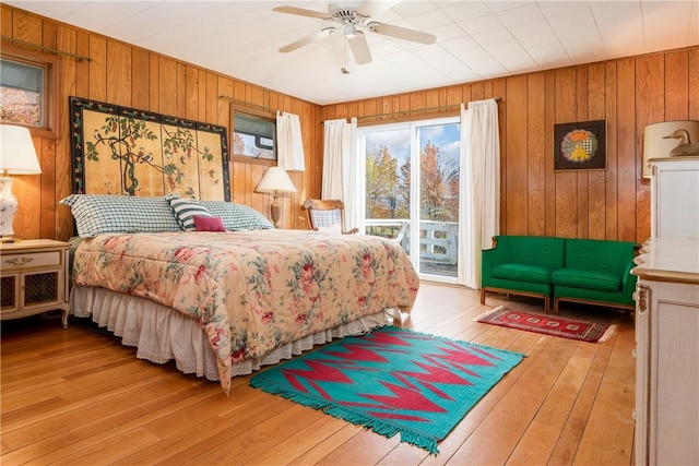 bedroom featuring access to outside, hardwood / wood-style flooring, wooden walls, and ceiling fan