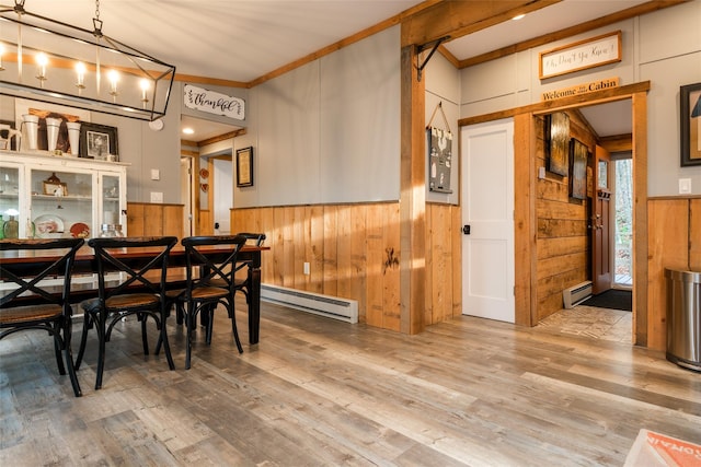 dining area featuring wooden walls, hardwood / wood-style flooring, crown molding, and a baseboard heating unit