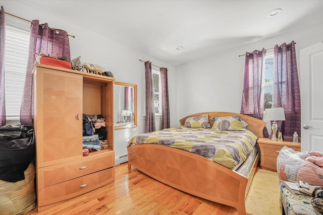 bedroom featuring baseboard heating, multiple windows, and light hardwood / wood-style floors