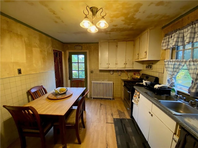 kitchen featuring radiator heating unit, black range oven, sink, light hardwood / wood-style floors, and white cabinets