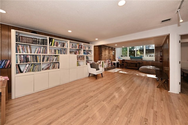 living area with wood walls, light wood-type flooring, and a textured ceiling