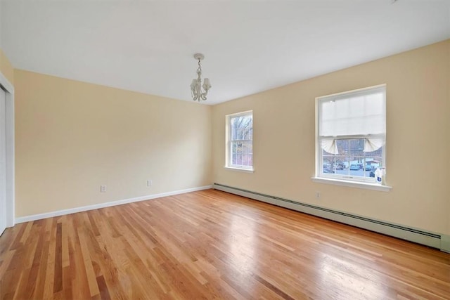 empty room featuring light hardwood / wood-style flooring, baseboard heating, and a notable chandelier