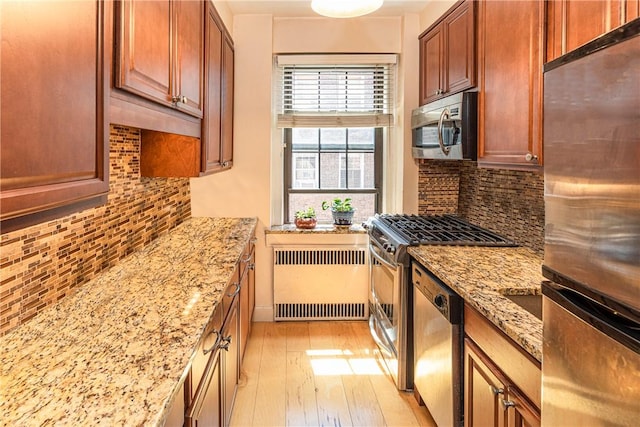 kitchen featuring radiator, tasteful backsplash, light stone counters, appliances with stainless steel finishes, and light wood-type flooring