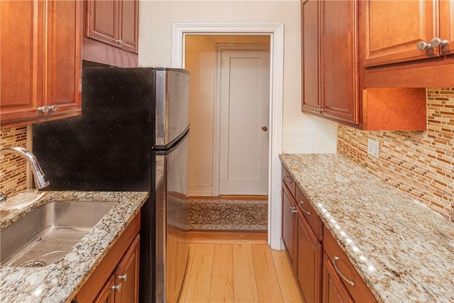 kitchen with backsplash, light hardwood / wood-style floors, light stone counters, and sink