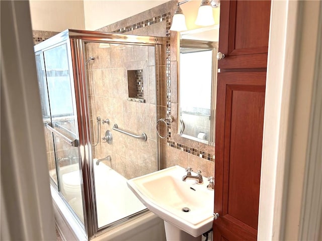 bathroom with tasteful backsplash, sink, and combined bath / shower with glass door