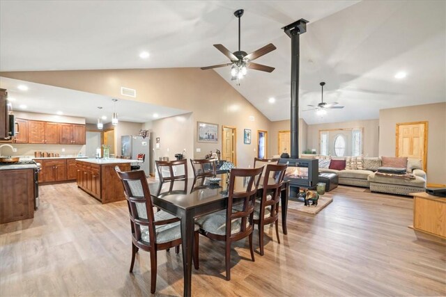 dining area featuring ceiling fan, light hardwood / wood-style floors, a wood stove, and high vaulted ceiling