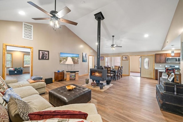 living room featuring a wood stove, plenty of natural light, high vaulted ceiling, and light wood-type flooring