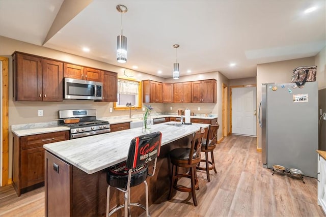 kitchen with pendant lighting, a breakfast bar, a kitchen island with sink, appliances with stainless steel finishes, and light hardwood / wood-style floors