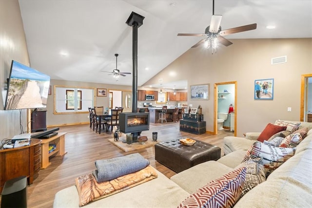 living area featuring high vaulted ceiling, a ceiling fan, a wood stove, and light wood-style floors