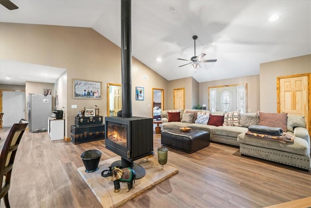 living room featuring a ceiling fan, a wood stove, high vaulted ceiling, and wood finished floors