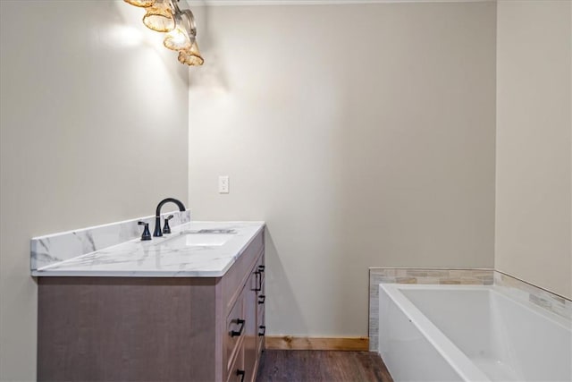 bathroom featuring a garden tub, baseboards, wood finished floors, and vanity