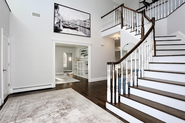 entryway with a towering ceiling, a baseboard heating unit, and dark hardwood / wood-style flooring