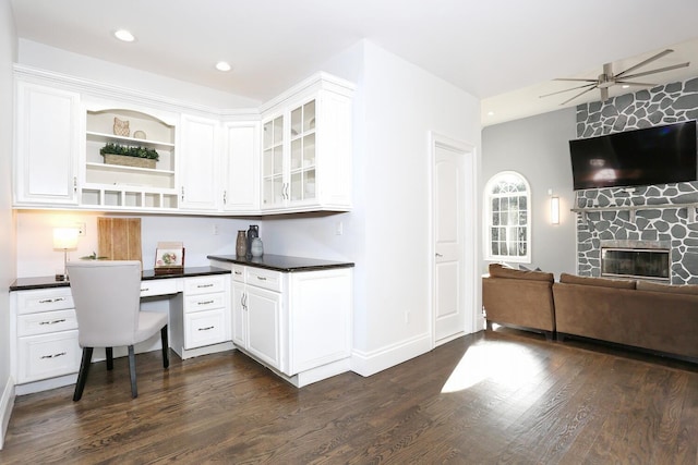 kitchen with white cabinets, dark hardwood / wood-style flooring, a stone fireplace, and built in desk