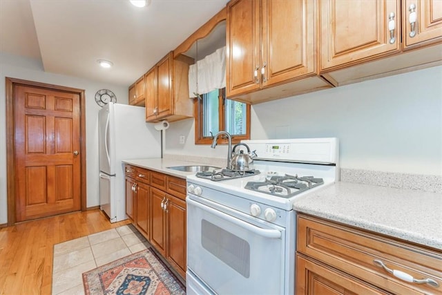 kitchen with decorative light fixtures, white appliances, sink, and light hardwood / wood-style flooring