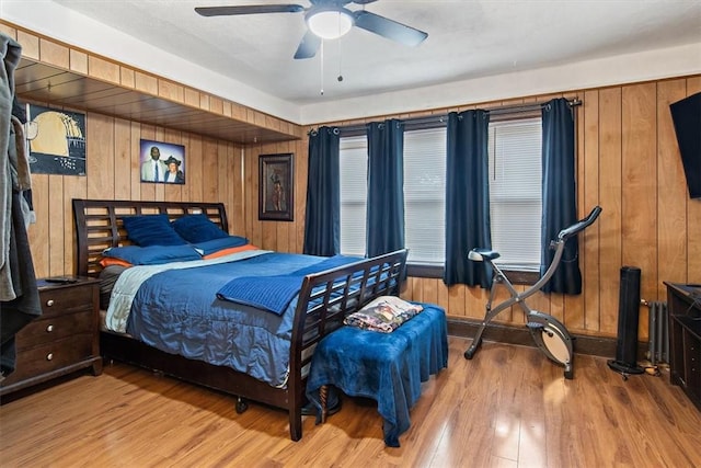 bedroom with ceiling fan, wooden walls, and light hardwood / wood-style flooring