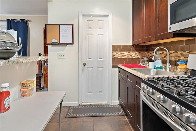 kitchen with sink, decorative backsplash, appliances with stainless steel finishes, dark tile patterned flooring, and ornamental molding