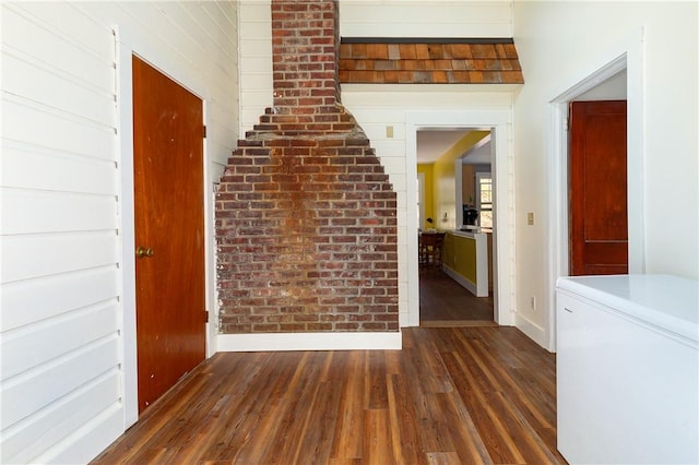 corridor with dark wood-type flooring and brick wall