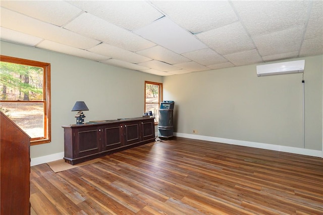 interior space featuring wood-type flooring, dark brown cabinetry, a wall unit AC, and a drop ceiling