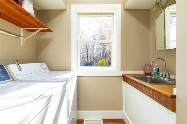 clothes washing area with washing machine and clothes dryer, hardwood / wood-style flooring, plenty of natural light, and sink