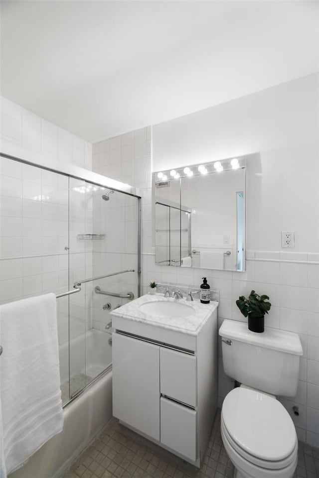 full bathroom featuring tile patterned floors, vanity, tile walls, enclosed tub / shower combo, and toilet