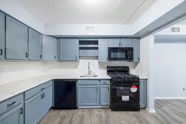 kitchen with black appliances, light wood-type flooring, sink, and a textured ceiling