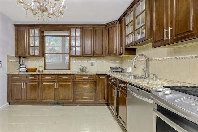 kitchen featuring backsplash, an inviting chandelier, sink, light stone counters, and stainless steel appliances