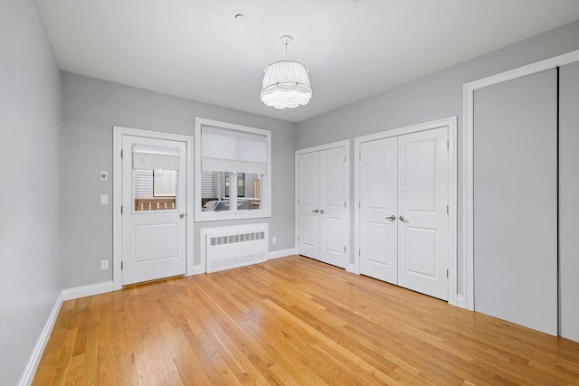 unfurnished bedroom featuring radiator, wood-type flooring, and two closets