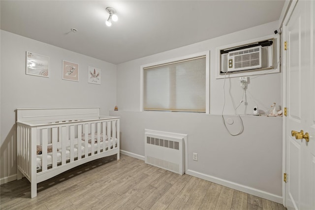 bedroom with a crib, radiator heating unit, a wall mounted AC, and light hardwood / wood-style flooring