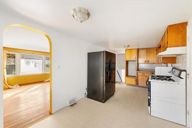 kitchen featuring decorative backsplash, light hardwood / wood-style floors, black fridge, and gas range gas stove