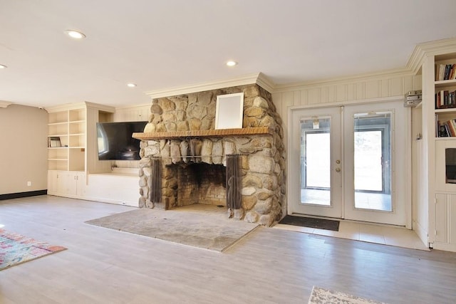 unfurnished living room featuring light hardwood / wood-style floors, a stone fireplace, crown molding, and french doors